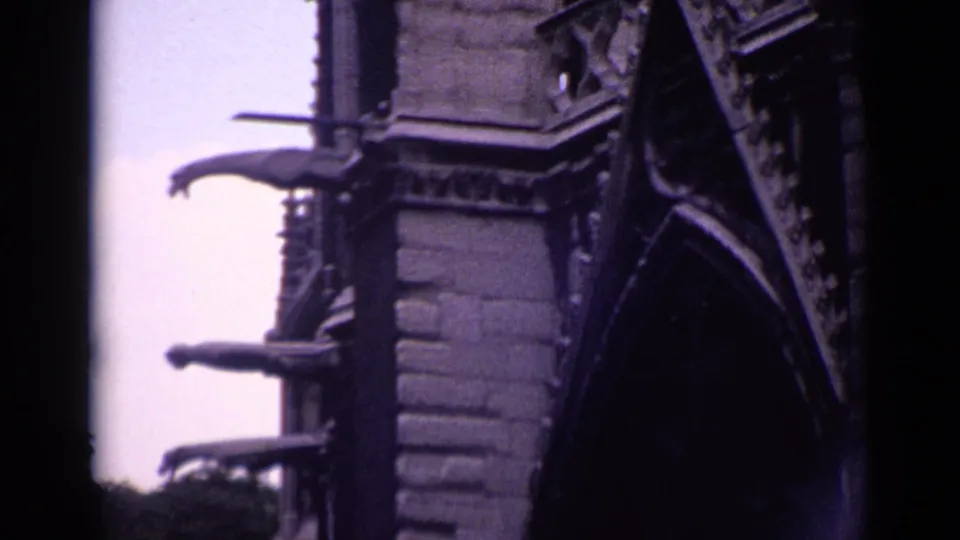 1962 Germany 8mm frame of Gothic-style church exterior details, with layered stone courses, pointed arch forms, and projecting spouts.