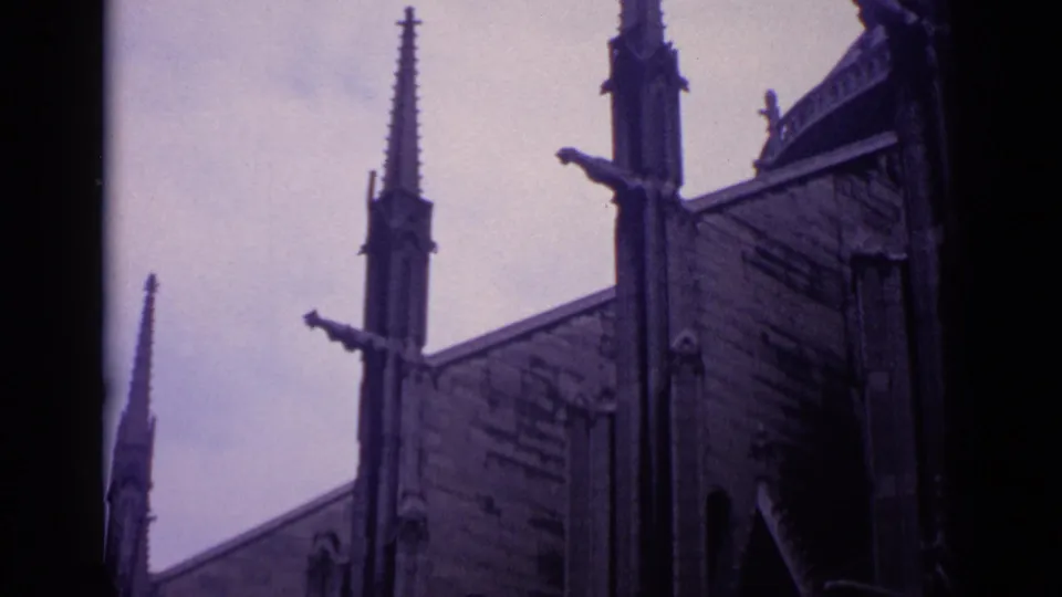 1962 Germany 8mm frame showing a tilted visitor view of a Gothic church roofline, tall spires, and ornamental stonework.