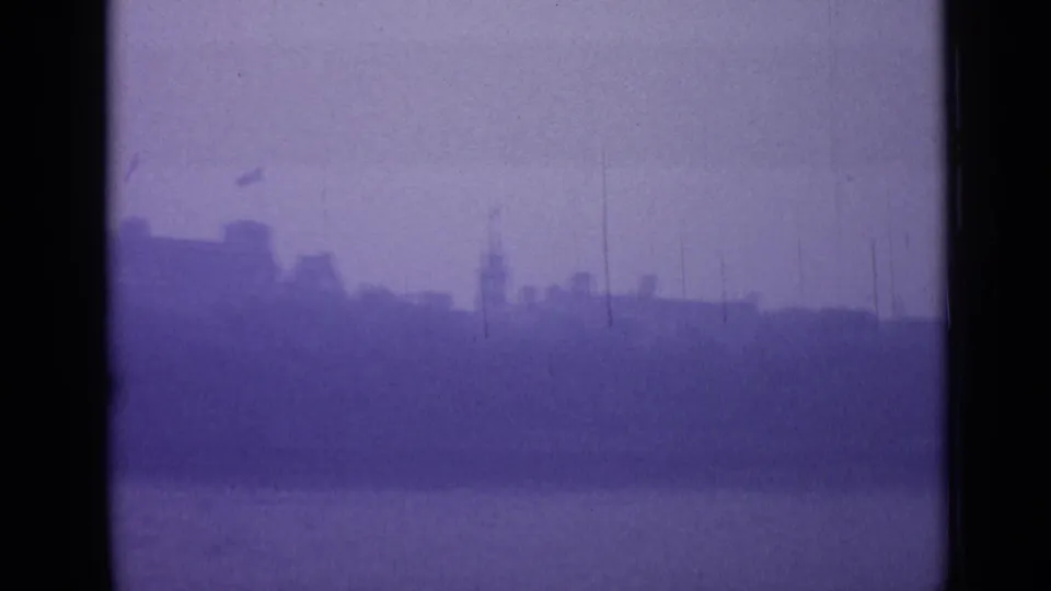 1962 London home-movie frame showing a hazy skyline across water, with distant building silhouettes and purple-blue film color shift.