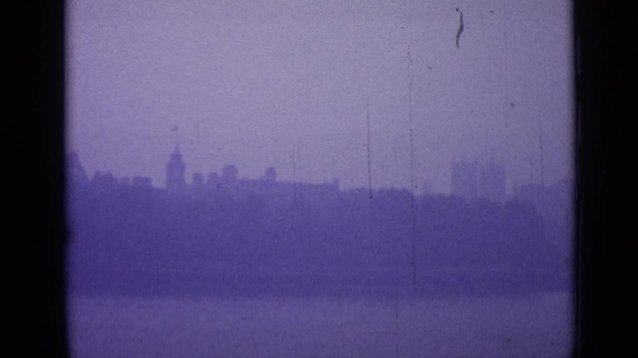 A distant London roofline appears through fog across water, with a tower silhouette softened by aged 8mm film texture.