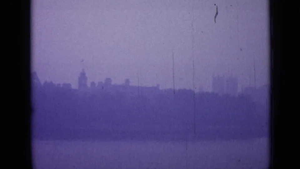 A distant London roofline appears through fog across water, with a tower silhouette softened by aged 8mm film texture.