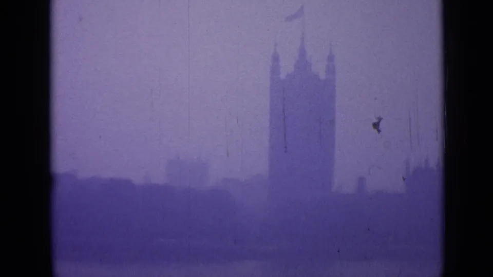 1962 London 8mm frame showing Westminster's tower silhouette through haze with purple tint, scratches and visible gate edges.