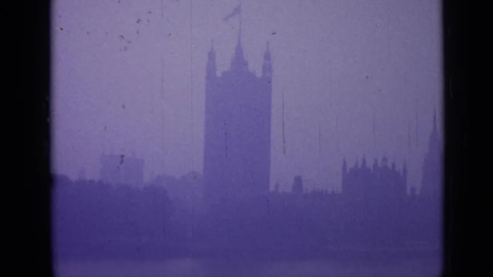 1962 London home-movie frame with the Palace of Westminster and Elizabeth Tower silhouetted against a foggy purple sky.