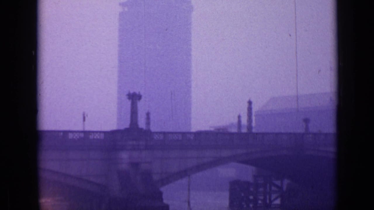 Stone bridge spans a river with a tall building rising in haze behind it.