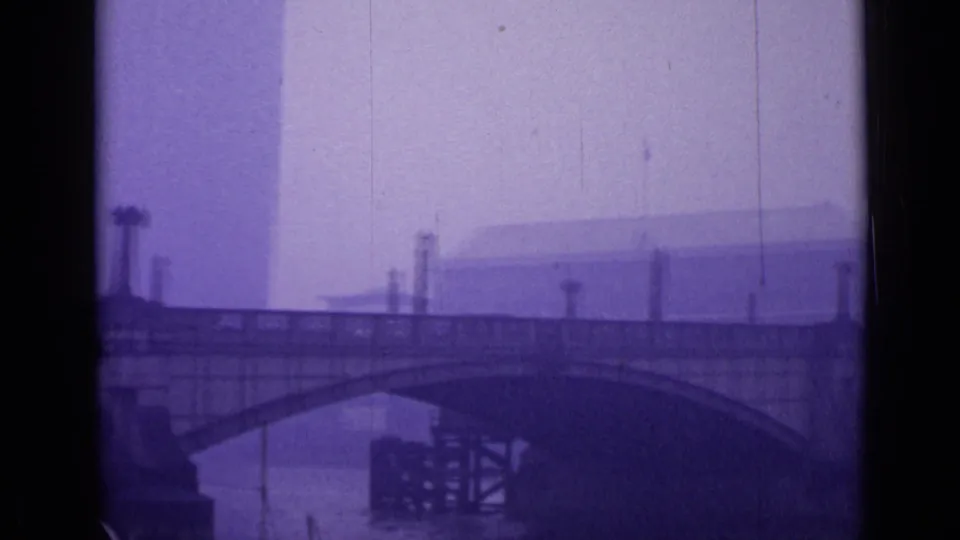 1962 London river bridge scene with a broad arch, waterfront structures, and tall forms softened by haze and film aging.