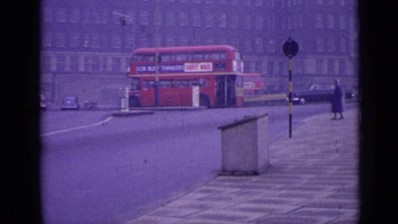 Red double-decker bus turns near a pedestrian island while cars and a walking figure appear nearby.