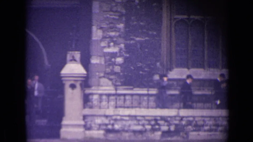 1962 London view of uniformed boys moving along a stone railing near an older building with dark stonework and tall windows.