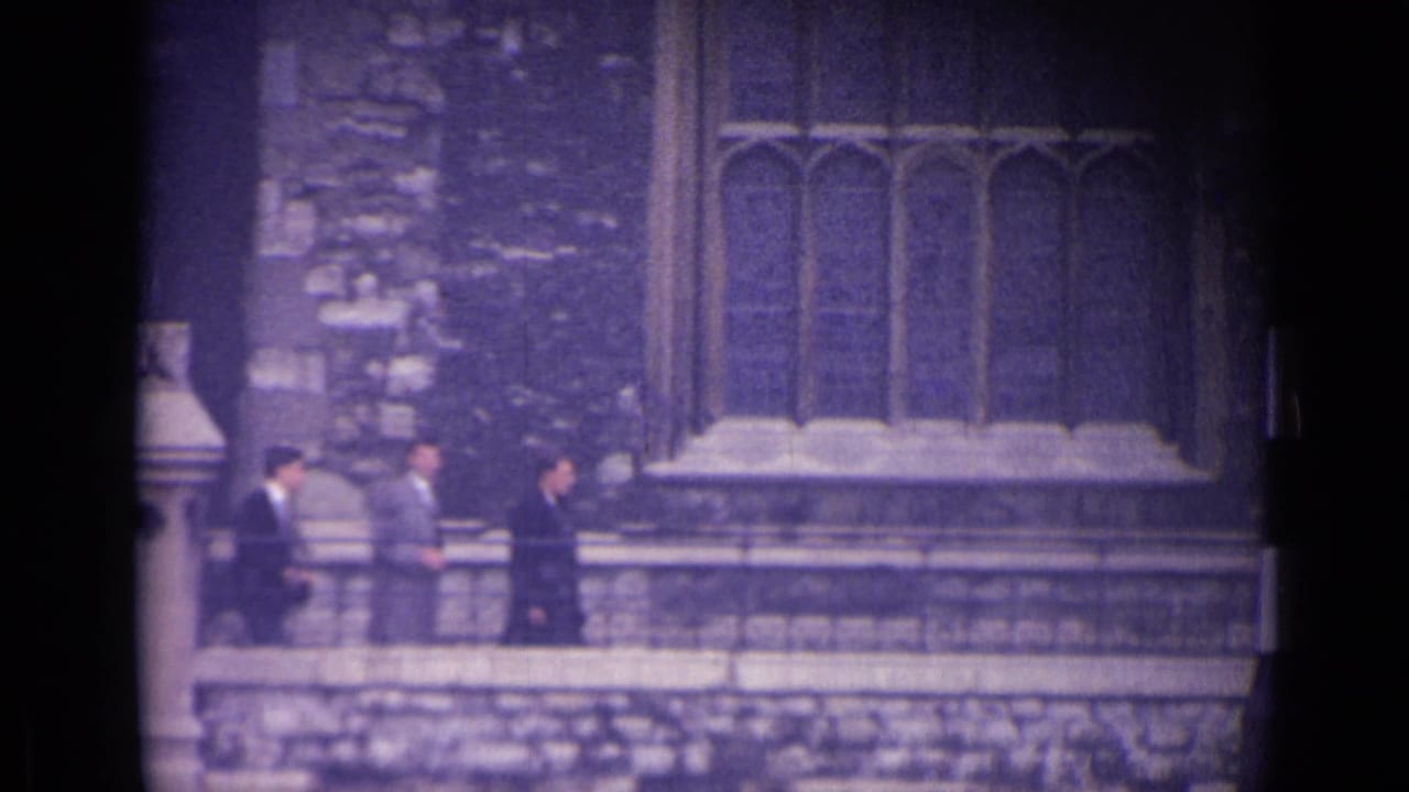 1962 London frame showing suited men walking past stonework and Gothic-style windows.