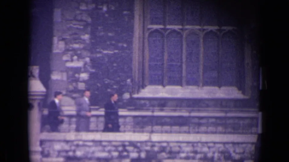 1962 London frame showing suited men walking past stonework and Gothic-style windows.