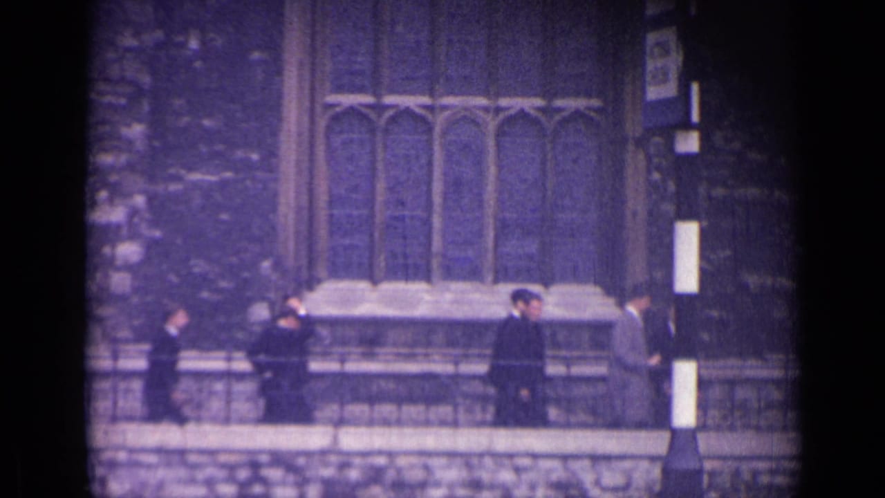 1962 London home-movie frame showing pedestrians near stone masonry, arched detail, and the edge of a grand building exterior.