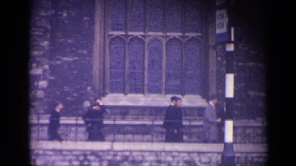 1962 London home-movie frame showing pedestrians near stone masonry, arched detail, and the edge of a grand building exterior.