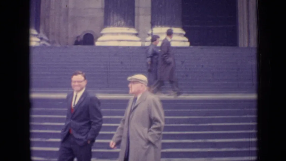 1962 London frame showing two men descending stone steps, with column bases and other passersby behind them.