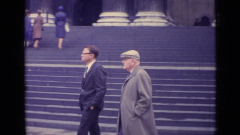 1962 London home-movie frame showing two men walking beside broad steps leading to a monumental columned building.