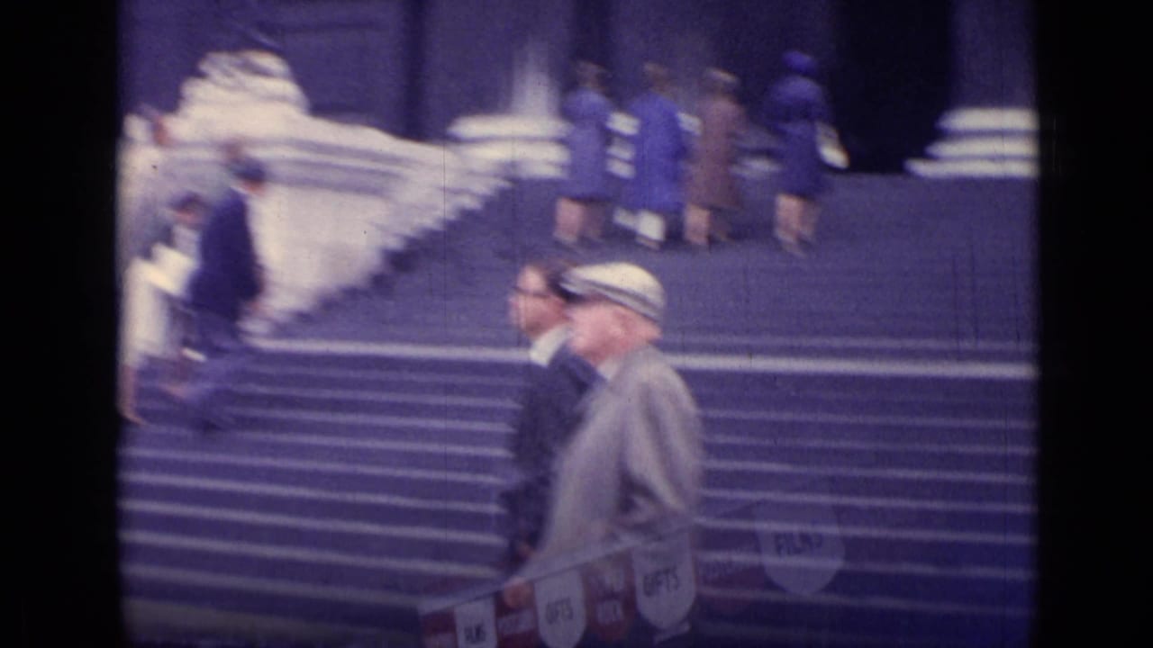 Two men walk in front of broad London steps while visitors and partial souvenir signs appear in the soft 8mm frame.