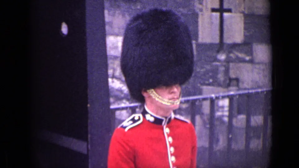 A closer 1962 London frame shows the ceremonial guard’s red tunic, chin strap, tall black hat, and nearby sentry box.