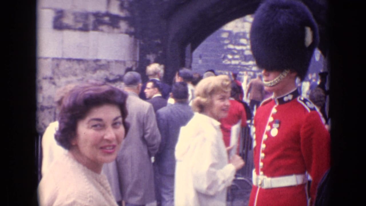 A woman in a light coat faces the camera as pedestrians gather near a red-uniformed guard under a London stone arch.
