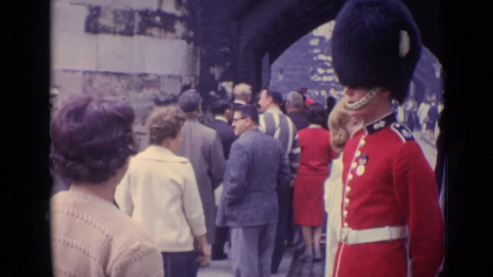 Pedestrians move through a stone passage while a London ceremonial guard in red uniform stands at the side of the frame.