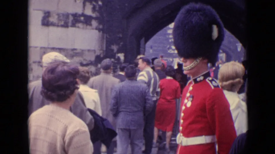 A red-uniformed ceremonial guard stands near the right edge as pedestrians walk beneath a London stone arch in 1960s footage.