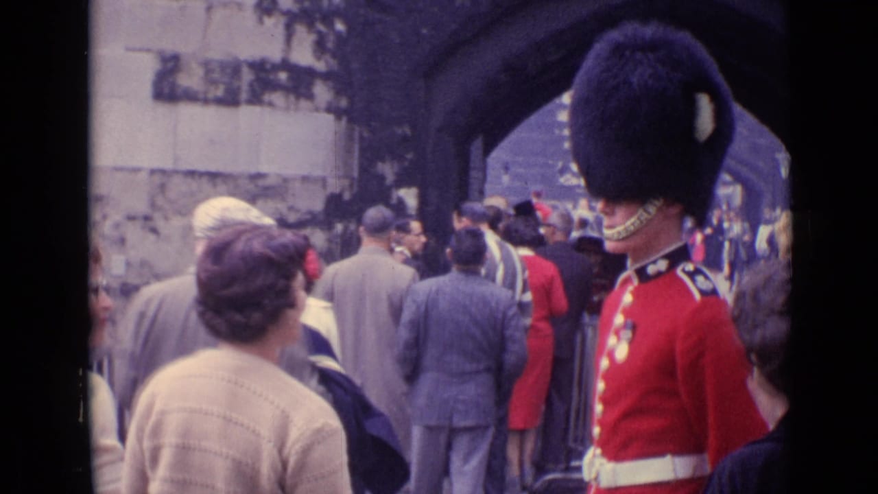 Tourists walk near a Royal Guard in a red tunic beneath stone arches.