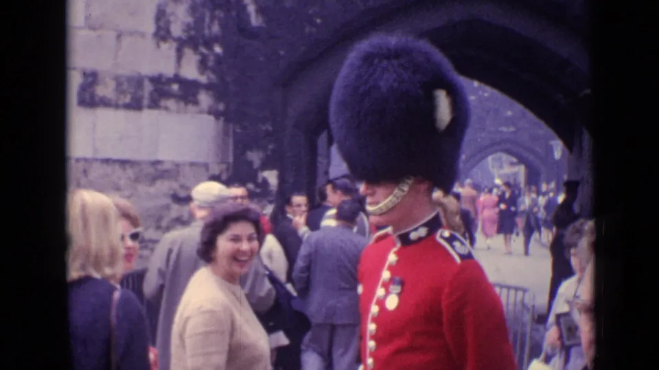 A woman smiles beside the ceremonial guard while tourists continue through the Tower of London passage.