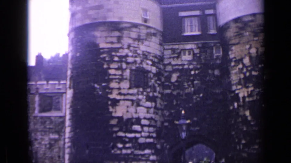 1962 8mm view of the Tower of London showing round stone towers, aged masonry, small windows and a cloudy sky.