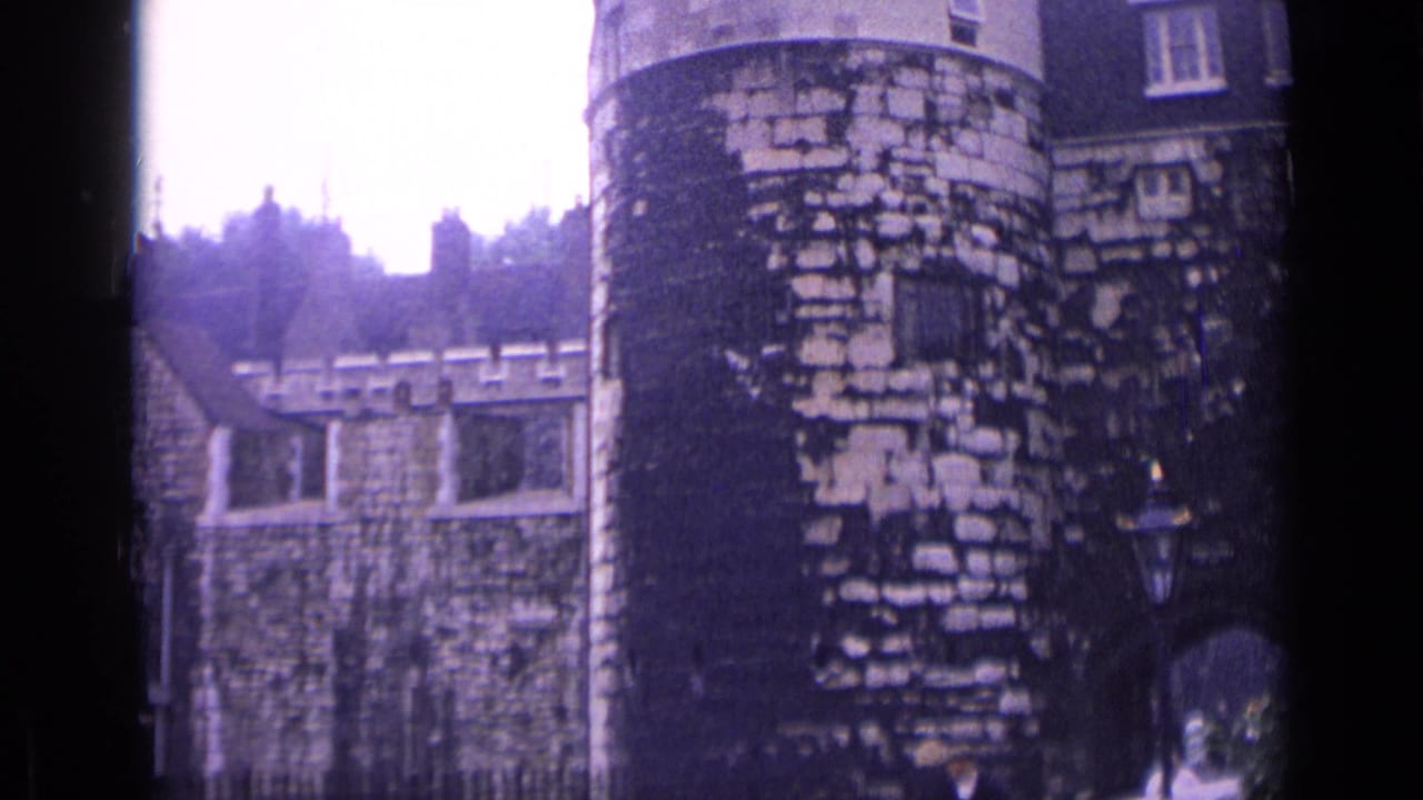 1962 London frame showing a Tower of London stone tower, crenellated wall, arched entry area and trees beyond.