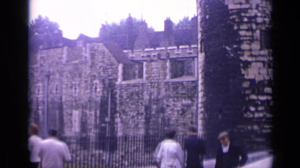 1962 visitor-shot London footage with people walking by an iron fence outside the Tower of London stone walls.