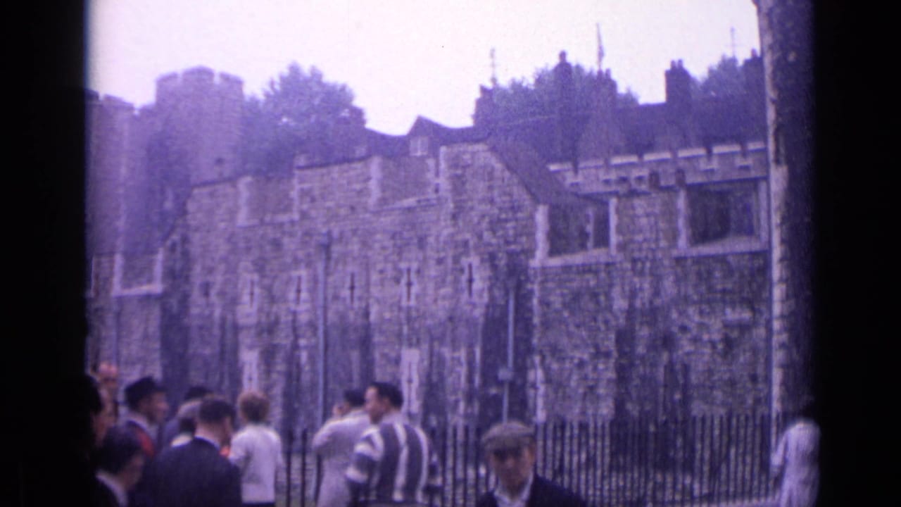 Tourists stand near an iron fence outside the Tower of London's stone walls.