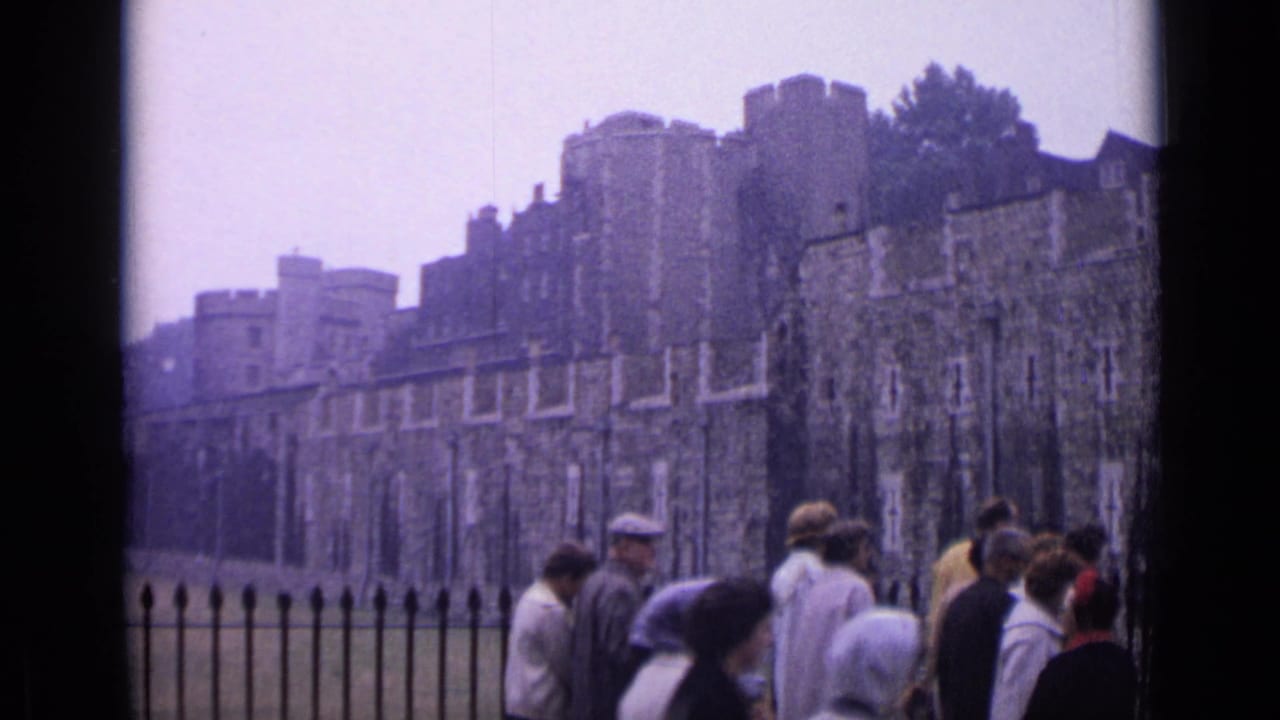 Tourists walk past an iron fence with Tower of London walls behind them.