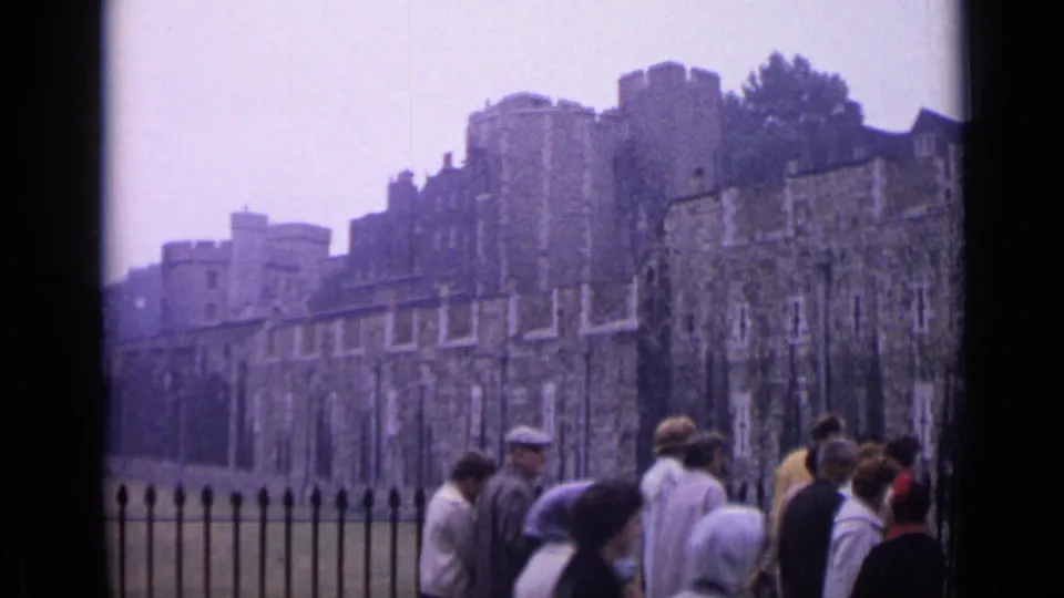 1962 London home-movie frame showing tourists near an iron fence in front of the Tower of London stone walls.