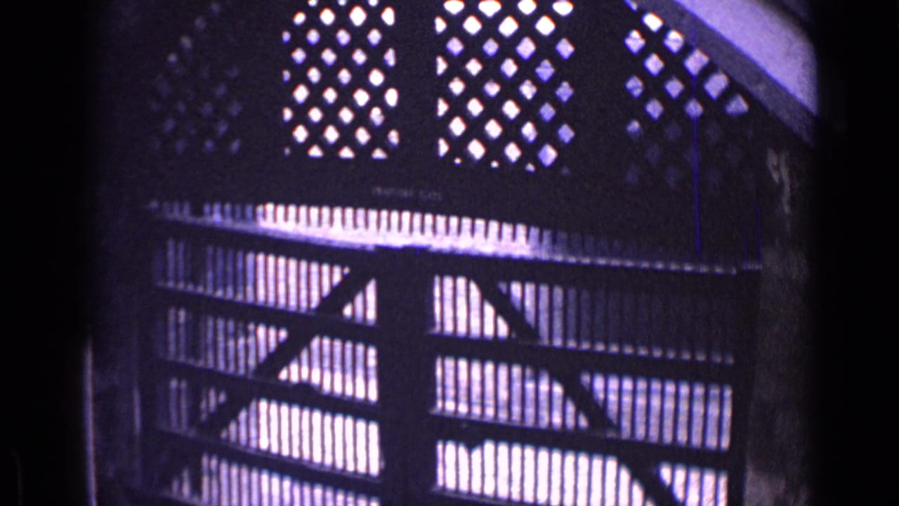 Dark gate with diamond lattice openings above vertical bars, lit from behind.