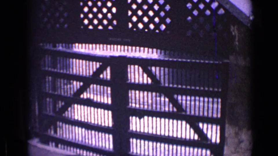 1962 London 8mm frame focused on the gate structure, showing vertical slats, diagonal supports, and a row of diamond openings above.