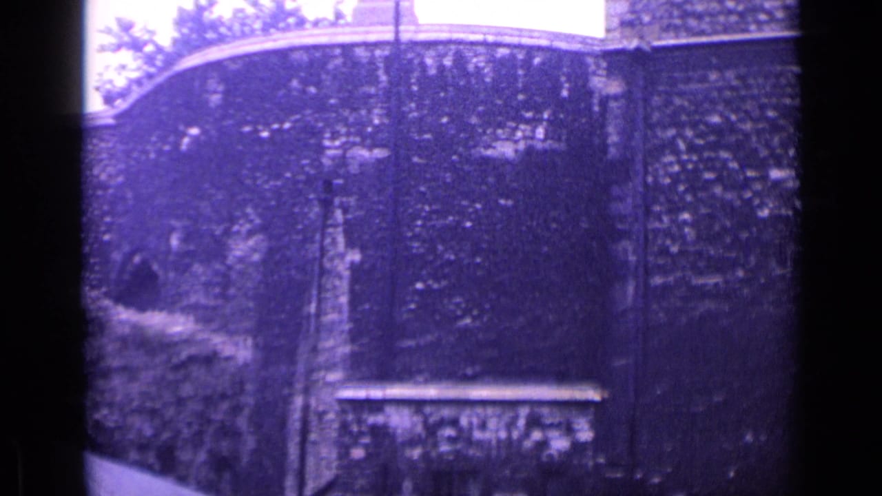 1962 London 8mm frame of a historic masonry exterior with arched openings, a bright glass-paned section, and cloudy sky.