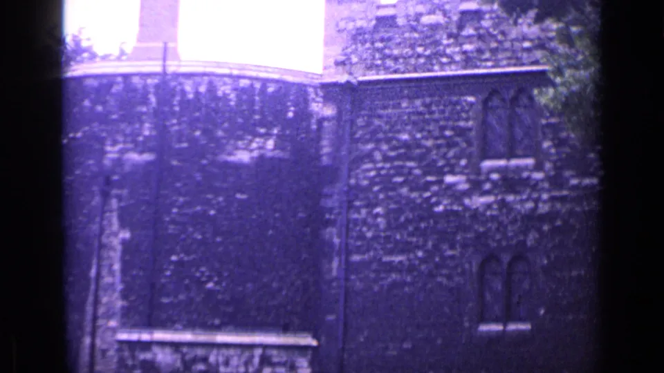 1962 London 8mm frame showing close masonry texture, arched windows, a bright upper opening, and purple-tinted film grain.