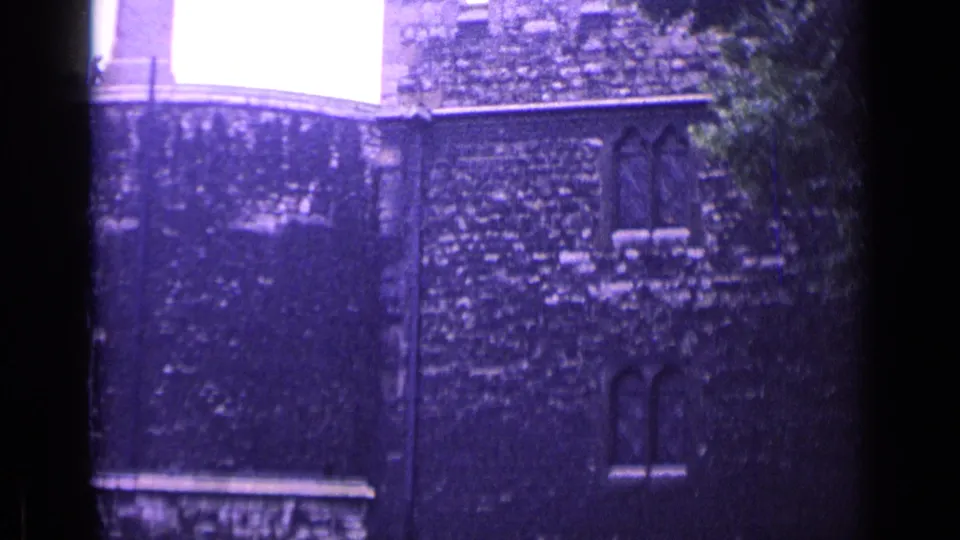 1962 London 8mm frame of a castle-like wall with arched windows, foliage at the side, and a bright glass-paned area above.