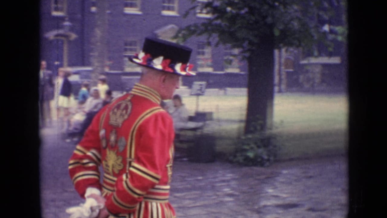 Uniformed man in a red coat and black hat walking beside a park path.
