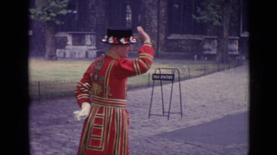 1962 London home-movie frame of a red-uniformed man gesturing near a NO ENTRY sign and cobblestone path.