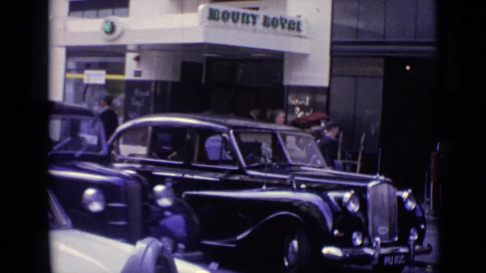 1962 London frame showing a black period car outside a building entrance marked Mount Royal, with people nearby.