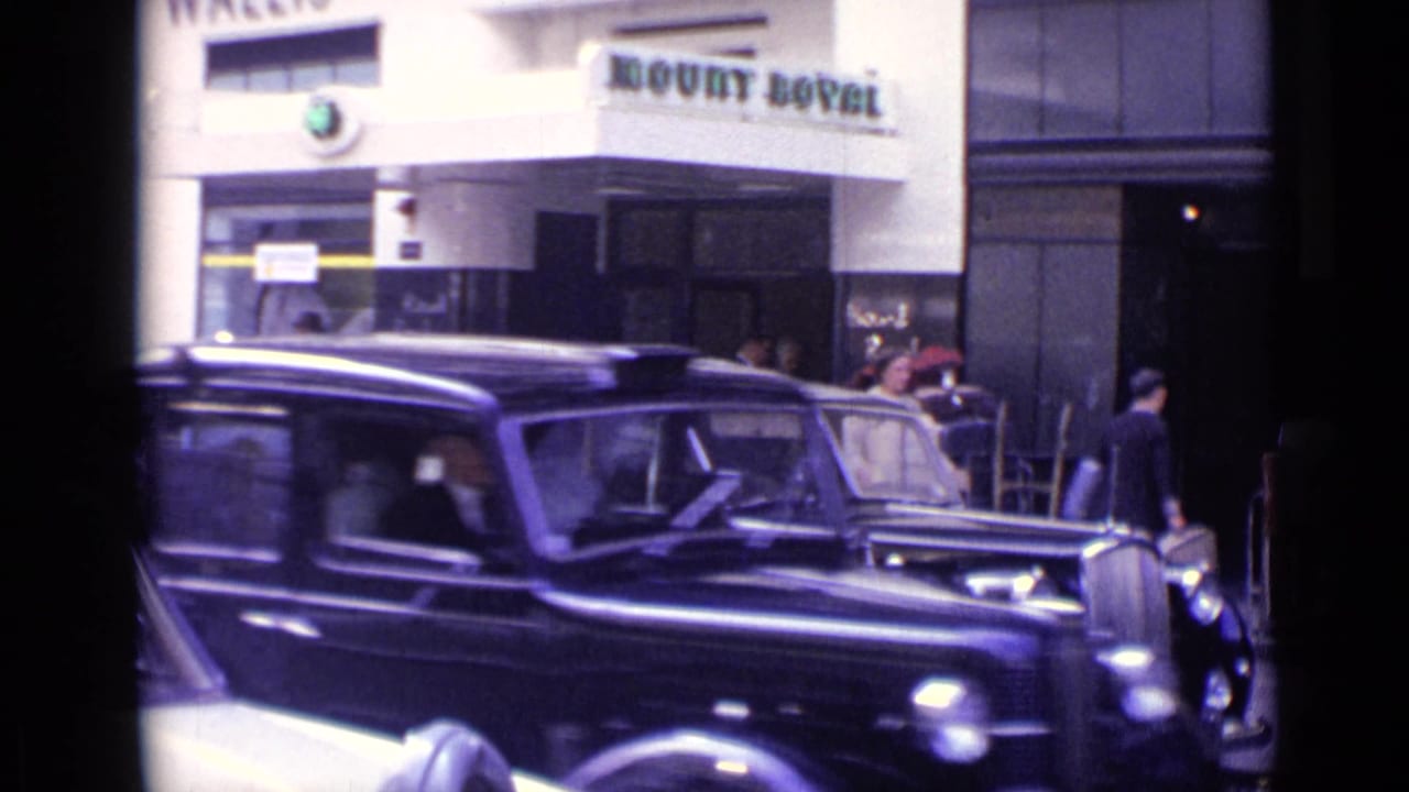 Black vintage limousine passing or parked outside Mount Royal frontage with pedestrians nearby.