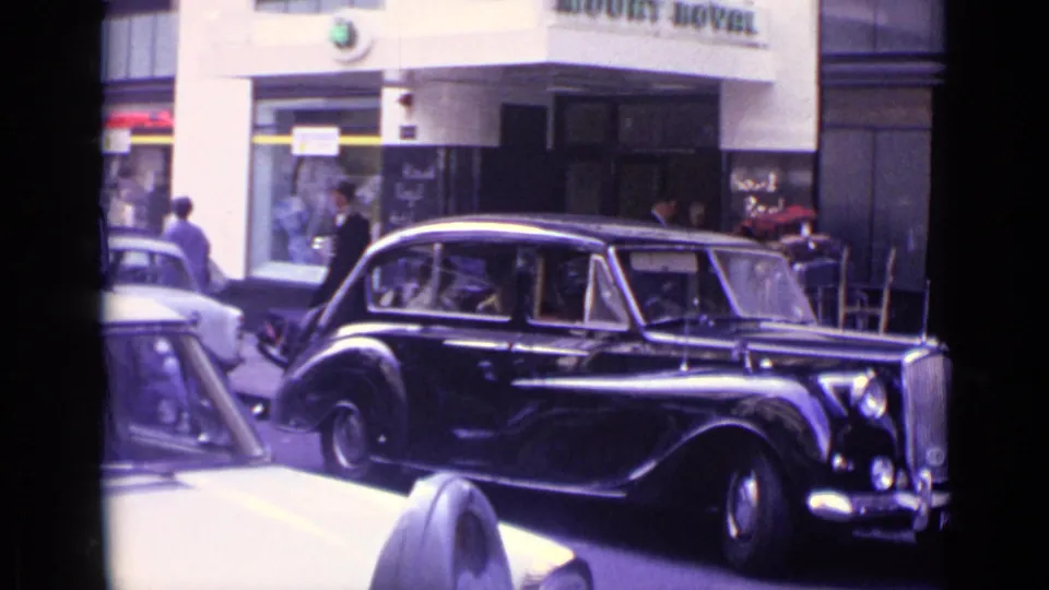 Final 1962 London street frame showing the black vintage limousine by the Mount Royal building with pedestrians and nearby vehicles.