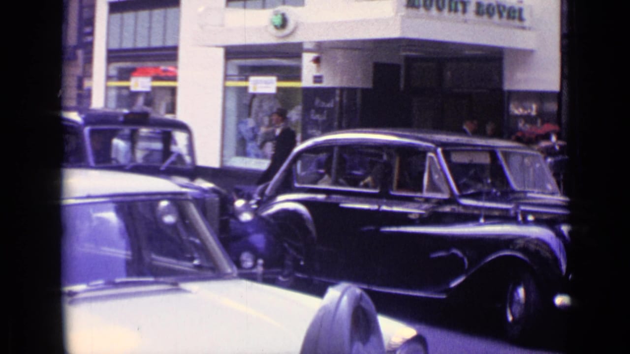 Classic cars in a London street near shopfronts and pedestrians.