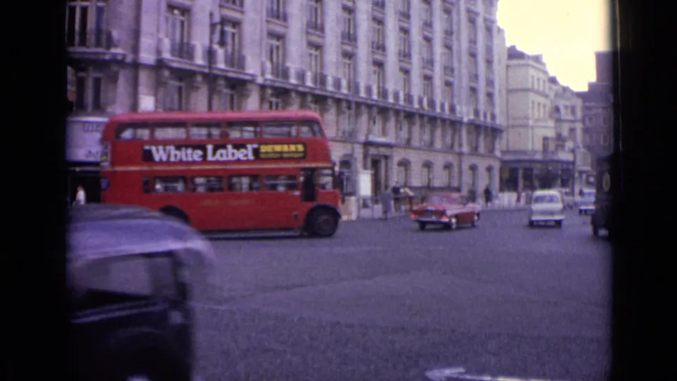 1962 London street scene with a red double-decker bus advertising White Label and cars passing tall buildings.