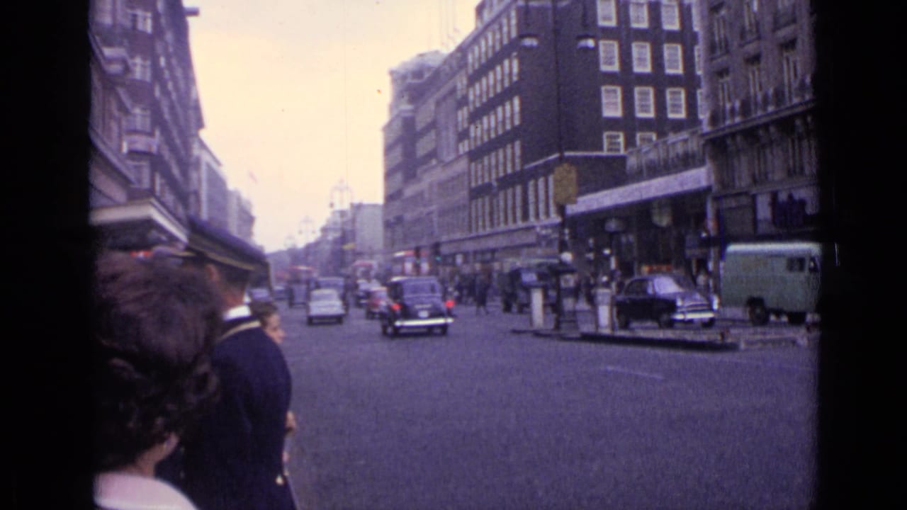 Cars, a van, and pedestrians move through a broad city street lined with buildings.