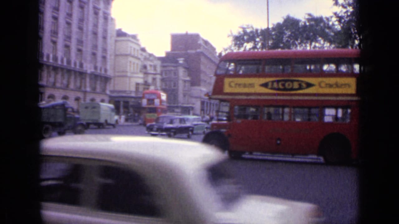 1962 London street view with a red double-decker bus, vintage cars, and period buildings seen from a handheld 8mm camera.