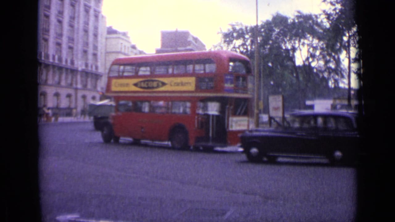 Red double-decker bus and black car on a broad city street near trees and buildings.