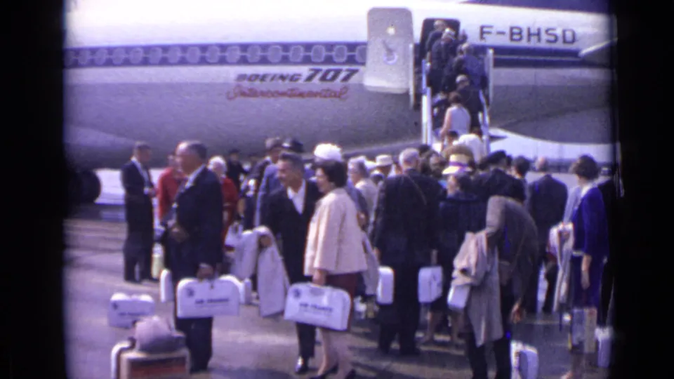 1962 London airport passengers in formal clothing wait beside a Boeing 707 Intercontinental while others board by stairs.