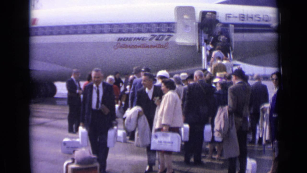 1962 London travelers in suits, hats, and coats queue with white luggage beside the Boeing 707 Intercontinental.