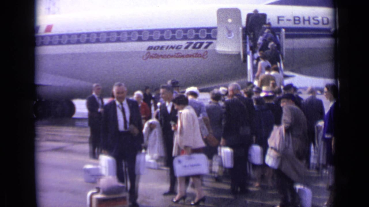 A tarmac boarding line at a London airport shows passengers with white luggage near an Air France Boeing 707.