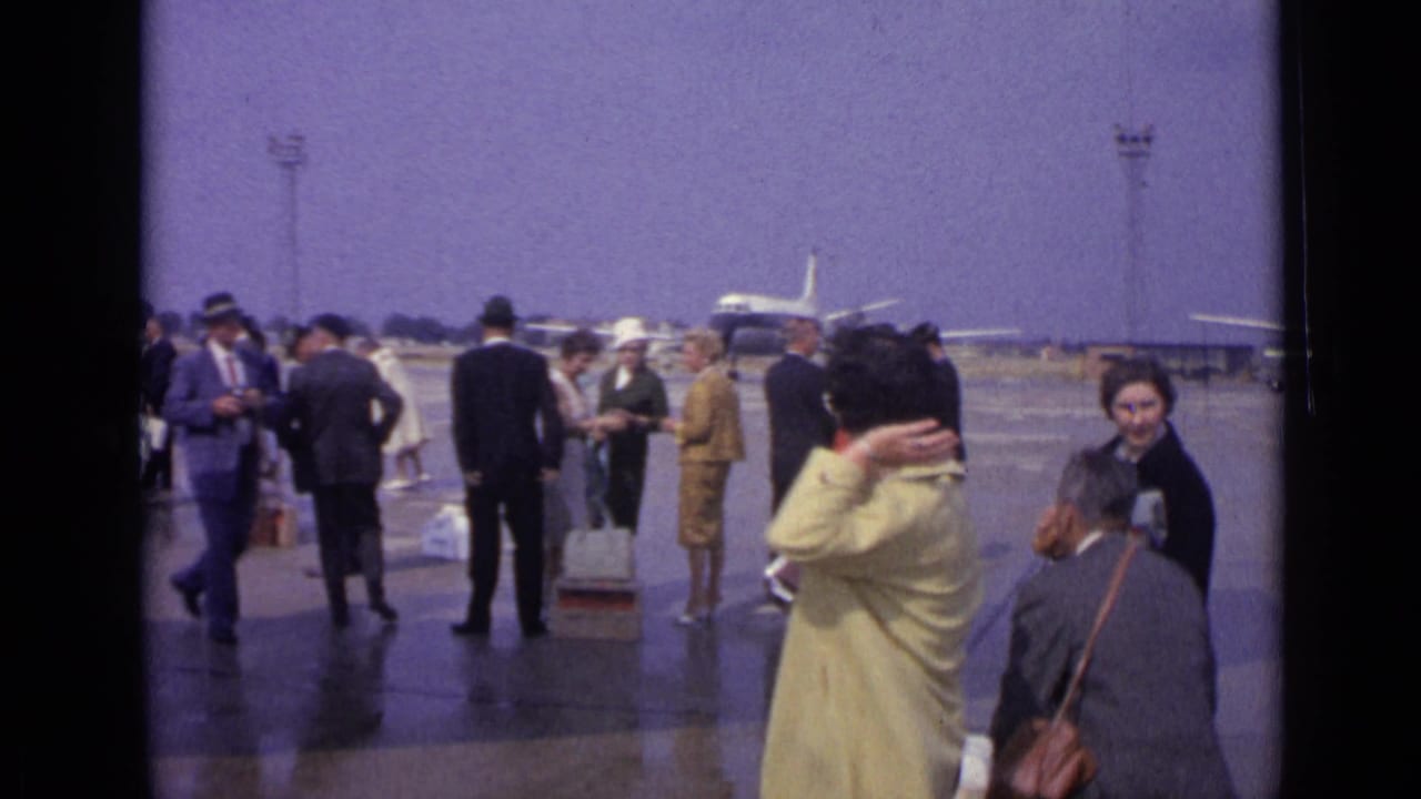 1962 London airport tarmac scene with travelers in coats and suits, luggage on the ground, and vintage airliners behind them.
