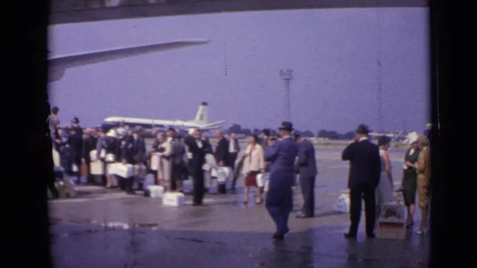 London 1962 airport footage showing travelers with luggage and uniformed personnel near a jet airliner on the apron.